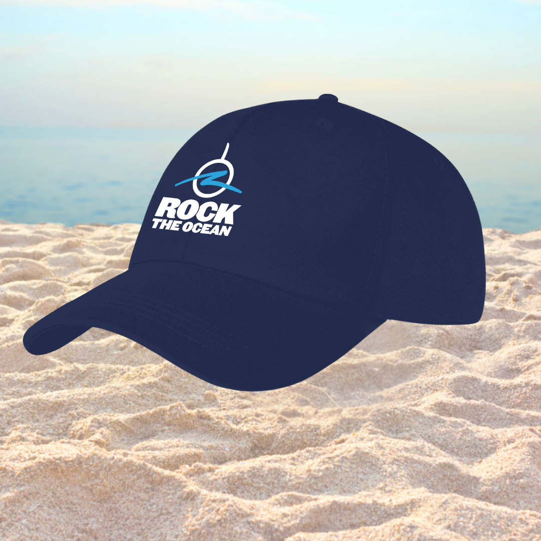 Navy blue cap with 'Rock the Ocean' logo on a sandy beach
