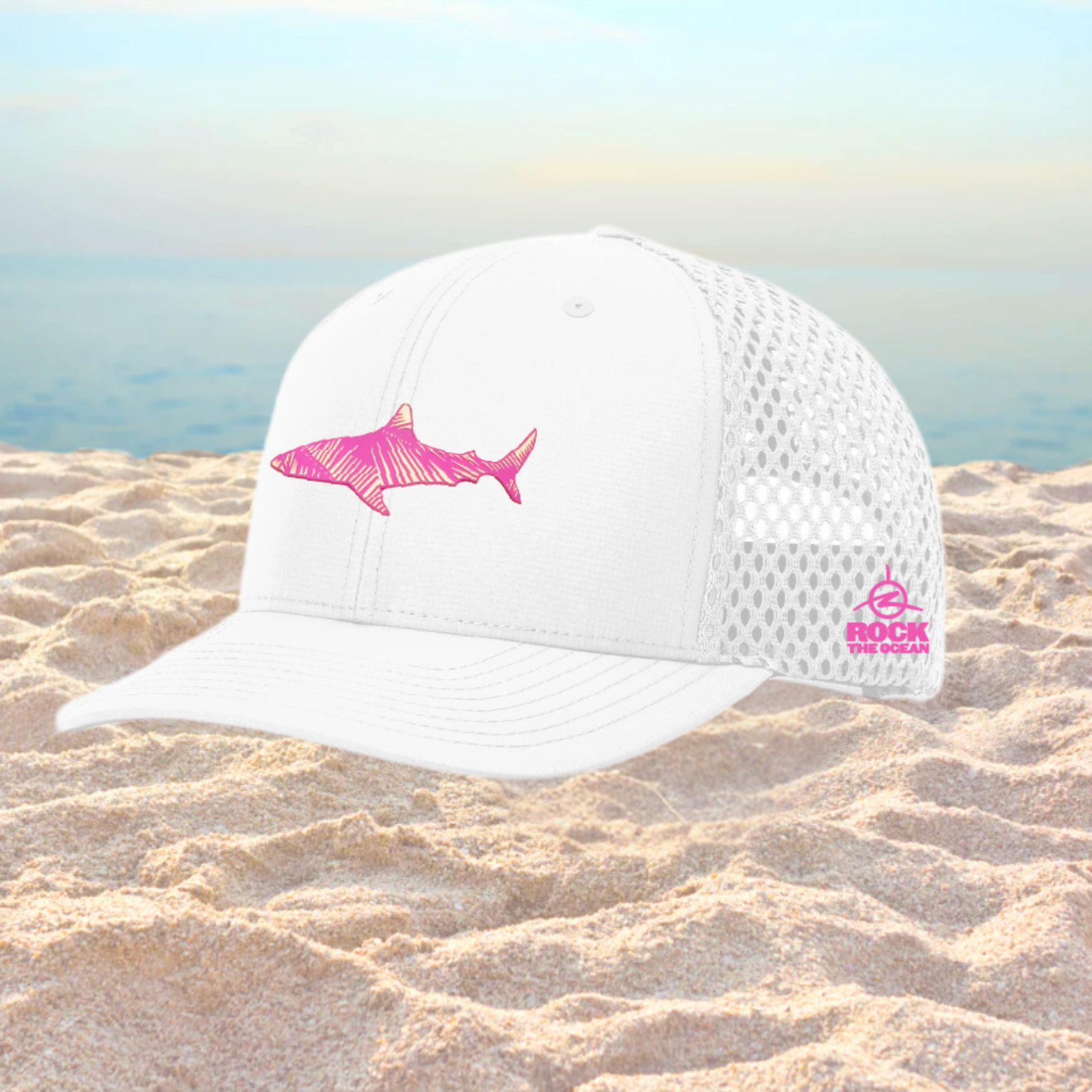 White cap with pink shark design on a sandy beach